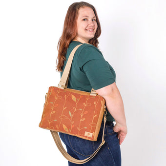 A woman carrying a brown convertible handbag with a leaf pattern and tan cotton straps named after Nita 