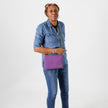 A woman wearing a purple crossbody pouch on a white background  named after Nora