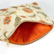 Orange textured interior of a floral-patterned pouch with a gold zipper on a white background
