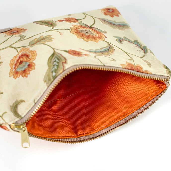 Orange textured interior of a floral-patterned pouch with a gold zipper on a white background