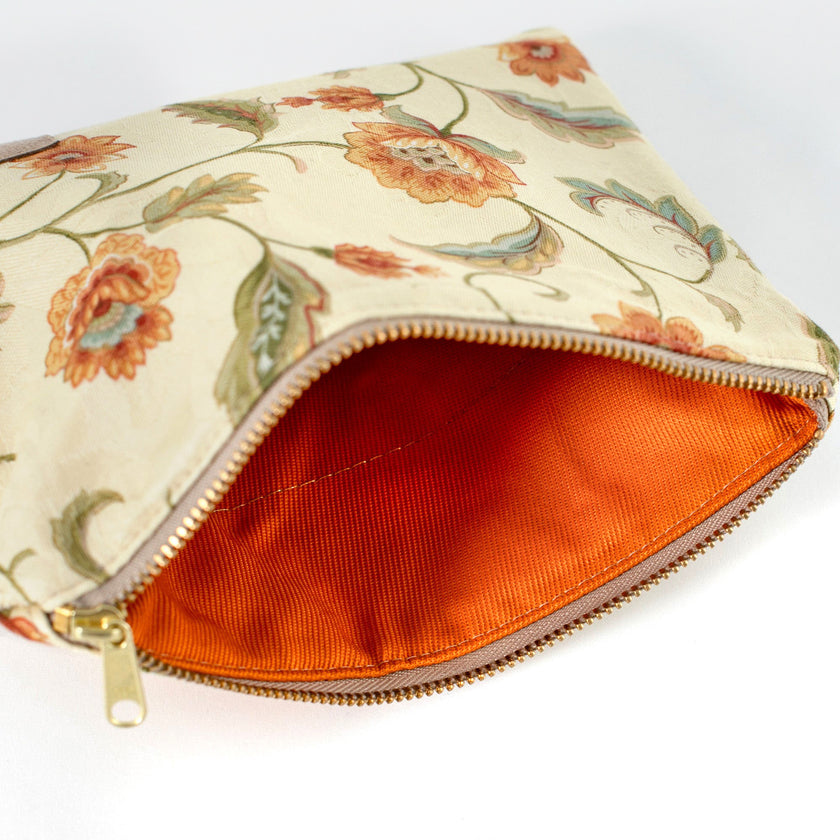 Orange textured interior of a floral-patterned pouch with a gold zipper on a white background
