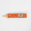 Bright and practical, this orange fabric wristlet key clip features a playful dotted pattern and sleek gold-tone hardware.