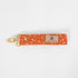 Bright and practical, this orange fabric wristlet key clip features a playful dotted pattern and sleek gold-tone hardware.