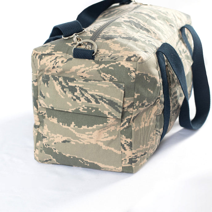 Original pocket from a US Airforce unform on a camouflage duffel bag with blue cotton straps on a white background