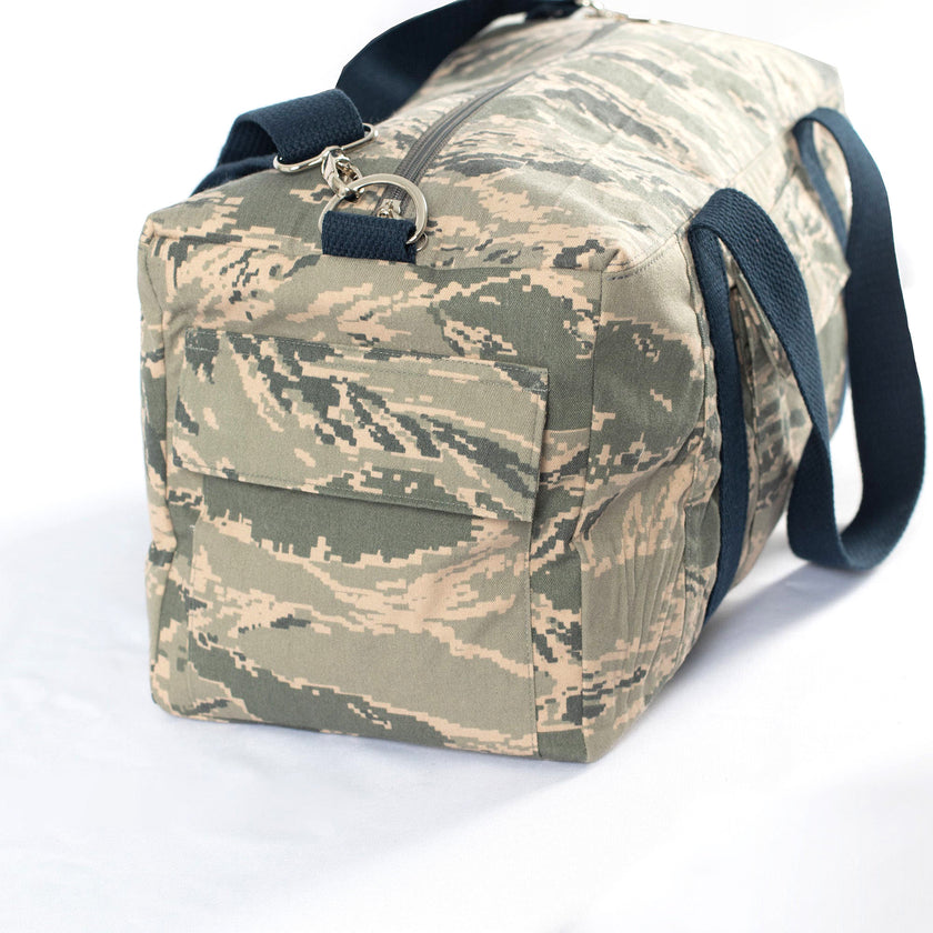 Original pocket from a US Airforce unform on a camouflage duffel bag with blue cotton straps on a white background