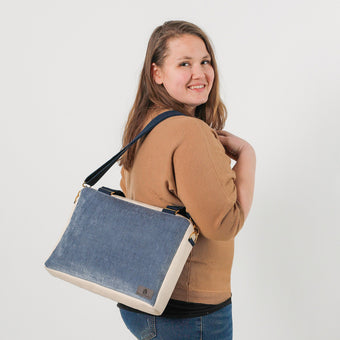 A woman carrying a blue and white convertible handbag with an adjustable strap, gold-tone hardware, and a zipper closure named after Pam.