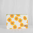 A large zip pouch with a white background and a vibrant floral pattern, featuring yellow flowers with blue centers. The pouch has a gold-tone zipper and a brand label in the bottom right corner.