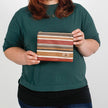 A woman holding a fall colored striped zip pouch named after Peanut