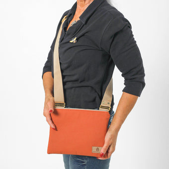 Person holding a handcrafted crossbody bag made from orange pebbled vegan leather with a beige strap on a white background
