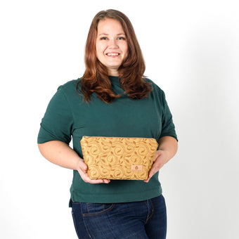Woman holding a yellow  ivy patterned fabric makeup kit against a plain background named after Priscilla
