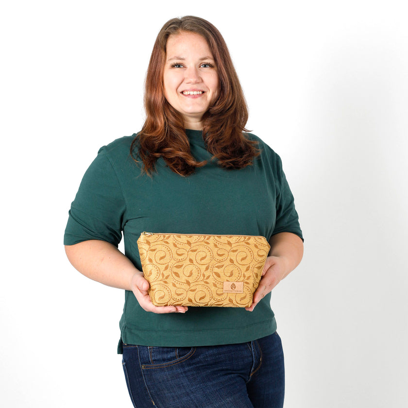 Woman holding a yellow  ivy patterned fabric makeup kit against a plain background named after Priscilla