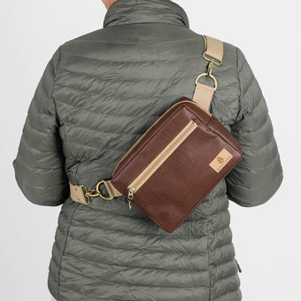 A woman wearing a brown luxury leather alternative errand bag with tan straps and gold hardware named after Priscilla