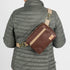 A woman wearing a brown luxury leather alternative errand bag with tan straps and gold hardware named after Priscilla