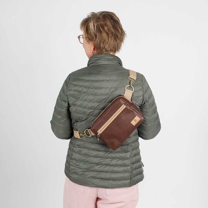 Person wearing a gray puffer jacket with a brown errand crossbody bag on a white background named after Priscilla
