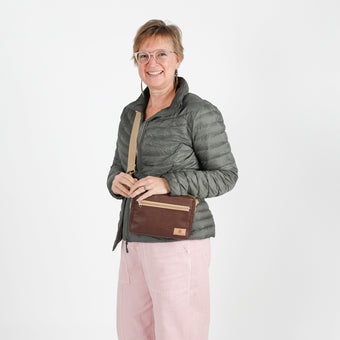 Woman wearing a gray puffer jacket with a brown errand crossbody bag on a white background named after Priscilla
