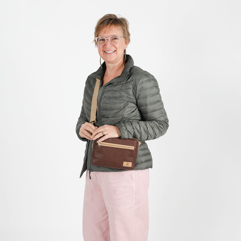 Woman wearing a gray puffer jacket with a brown errand crossbody bag on a white background named after Priscilla