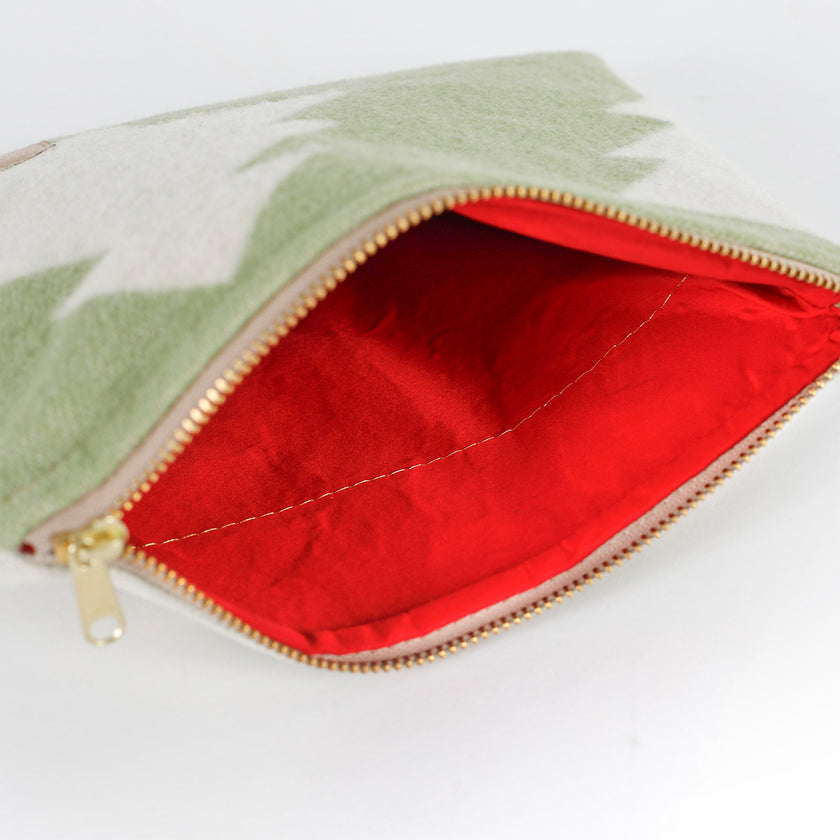 Red upcycled fabric interior of a green woolen pouch with a white Christmas tree pattern on a white background