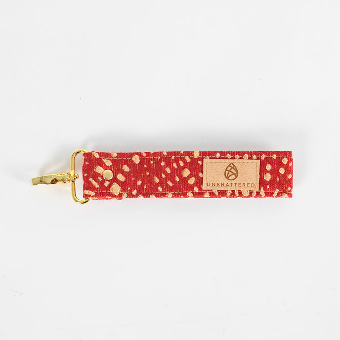 Bright and practical, this red fabric wristlet key clip features a playful dotted pattern and sleek gold-tone hardware.