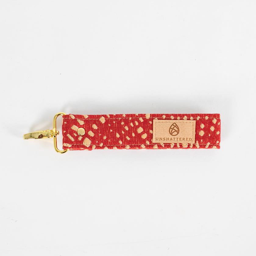 Bright and practical, this red fabric wristlet key clip features a playful dotted pattern and sleek gold-tone hardware.