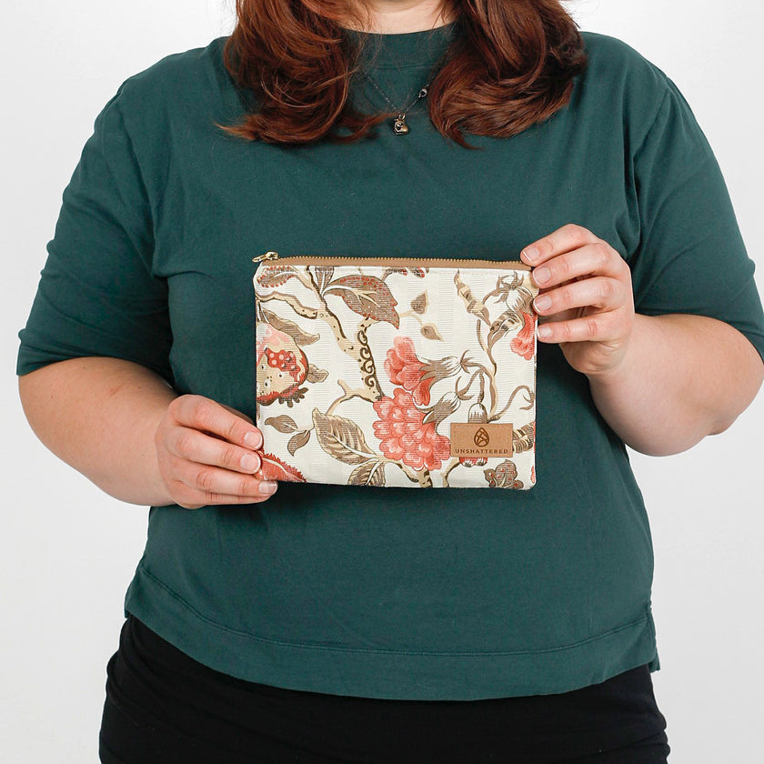 A woman holding a floral pattern zip pouch with a tan Unshattered label named after Reisha 
