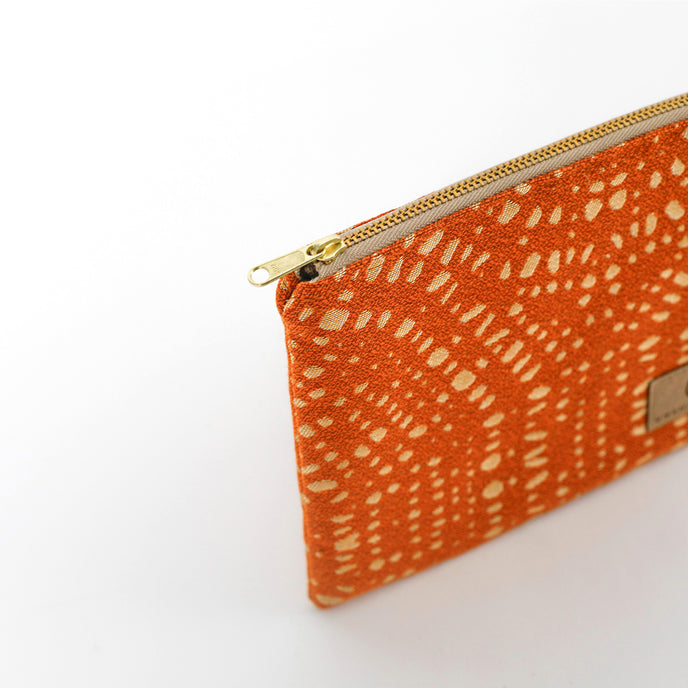 Orange pouch with white pattern and gold zipper on a light gray background named after Rena 