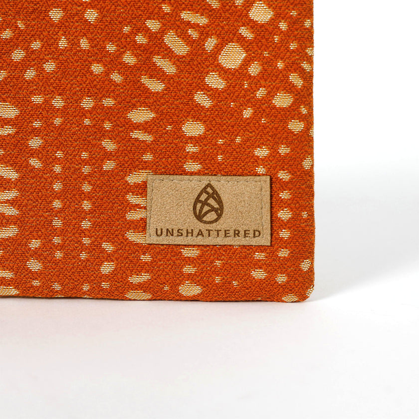 Orange fabric with a pattern zip pouch and 'Unshattered' brand label on a white background named after Rena 