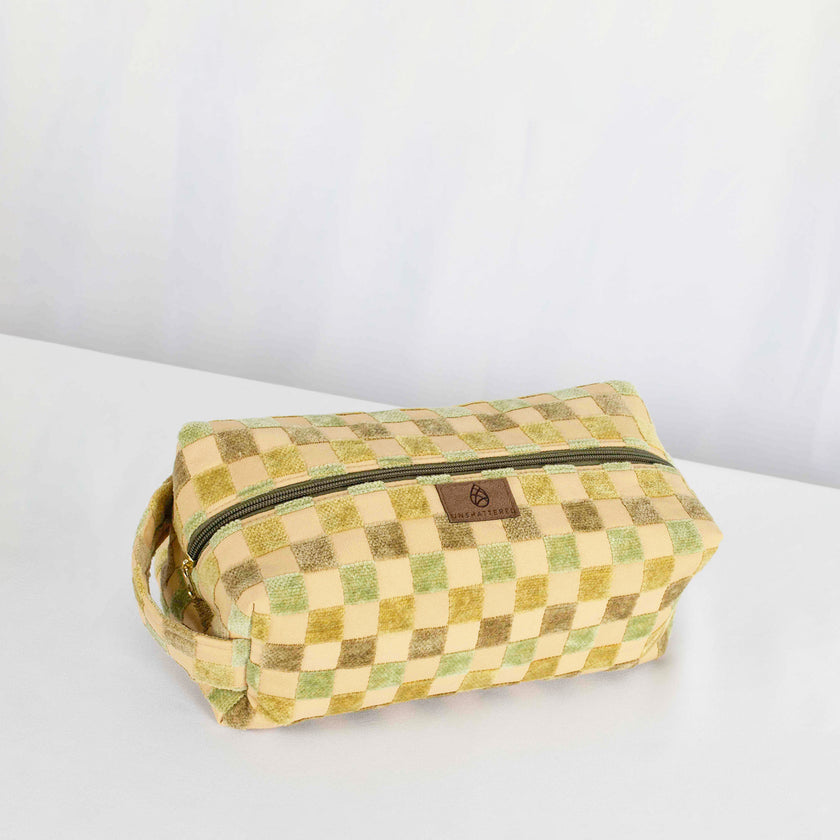 A  toiletry kit with a checkered pattern in green and tan colors, featuring a zip closure and gold-tone hardware.