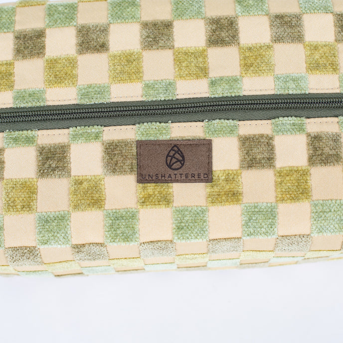 A close-up, detailed shot of a brown Unshattered brand label stitched onto the exterior of a stylish, upcycled checkered toiletry bag, showcasing the brand’s commitment to quality craftsmanship and sustainable material design.