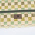 A close-up, detailed shot of a brown Unshattered brand label stitched onto the exterior of a stylish, upcycled checkered toiletry bag, showcasing the brand’s commitment to quality craftsmanship and sustainable material design.