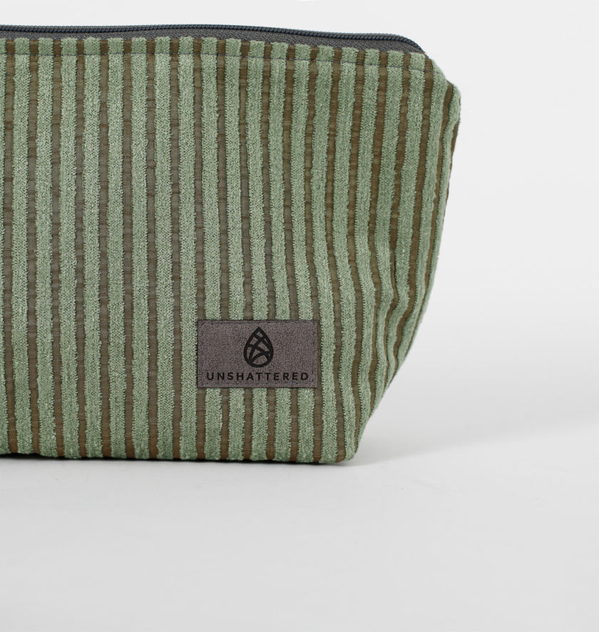 Close up of a gray ultrasuede Unshattered label on a green striped makeup kit. 