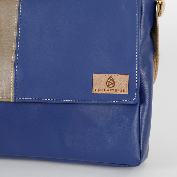 Blue leather bag with a 'Unshattered' brand label on a light gray background