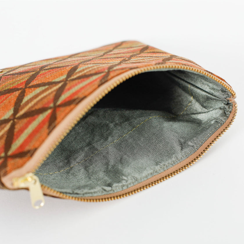 Light gray interior of a striped zippered pouch in autumnal colors with a prominent brown X overlay pattern on a white table. 
