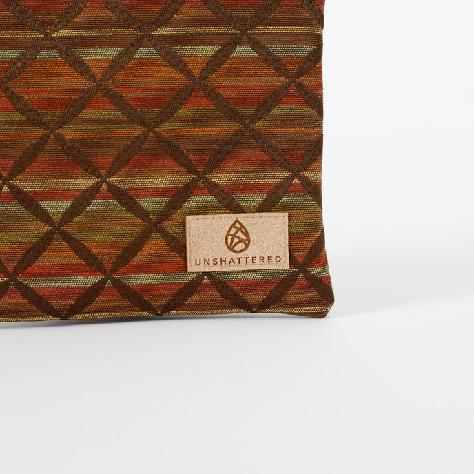 Close up of a tan suede Unshattered label on a striped zip pouch in autumnal colors.