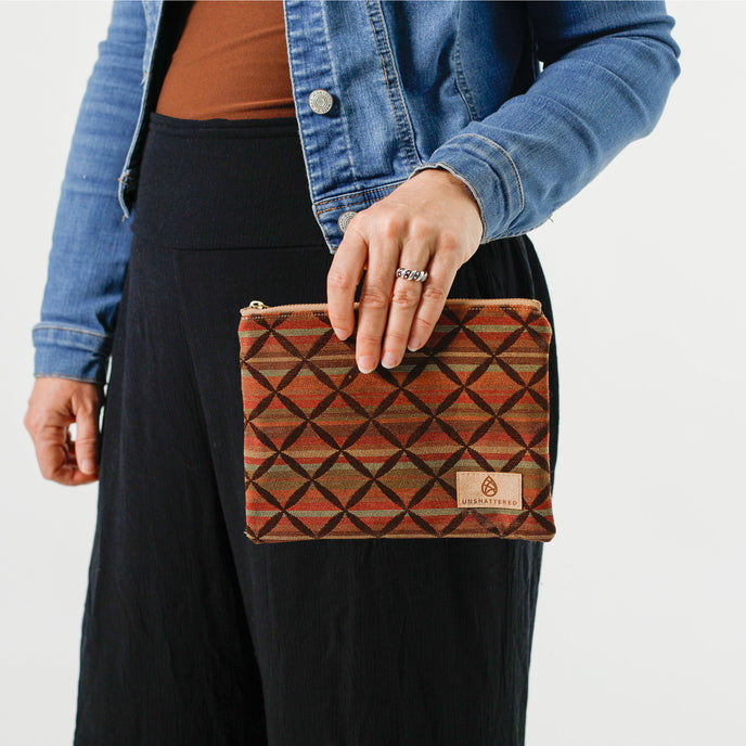 Person holding a striped zip pouch in autumnal colors with a prominent brown X overlay pattern.