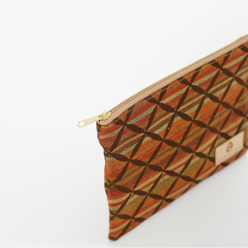 Gold-tone zipper on a striped zip pouch in autumnal colors with a prominent brown X overlay pattern on a white background