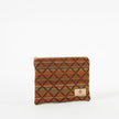 A geometric patterned zip pouch in autumnal colors with a prominent brown X pattern, featuring a small brand tag on the bottom right.