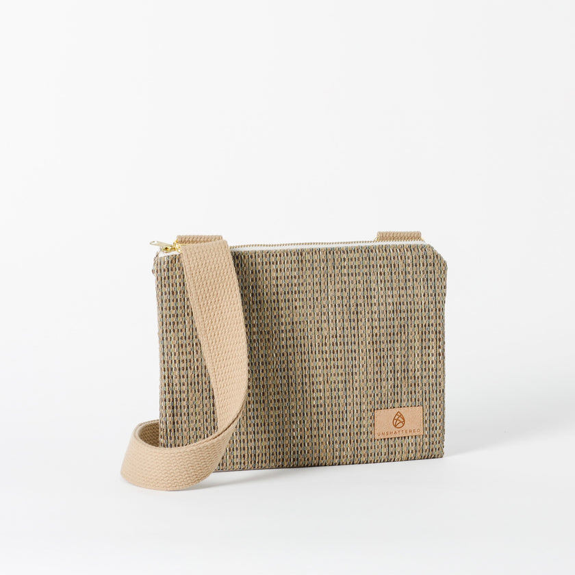 A beige and brown patterned crossbody pouch with a zipper and an adjustable strap, displayed against a plain background named after Shakira