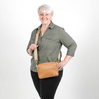 Woman holding a tan crossbody bag against a white background