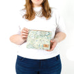 A woman holding a green, blue, and white  geometric shapes and design zip pouch bag named after Shelby 