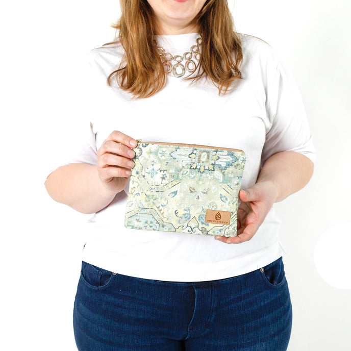 A woman holding a green, blue, and white  geometric shapes and design zip pouch bag named after Shelby 