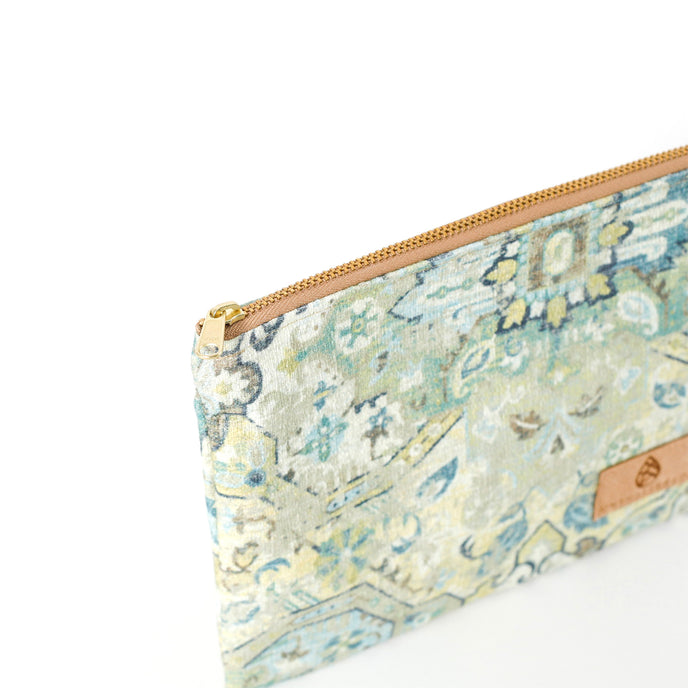 A gold toned zipper on a green, blue, yellow, and white zip pouch named afetr Shelby 