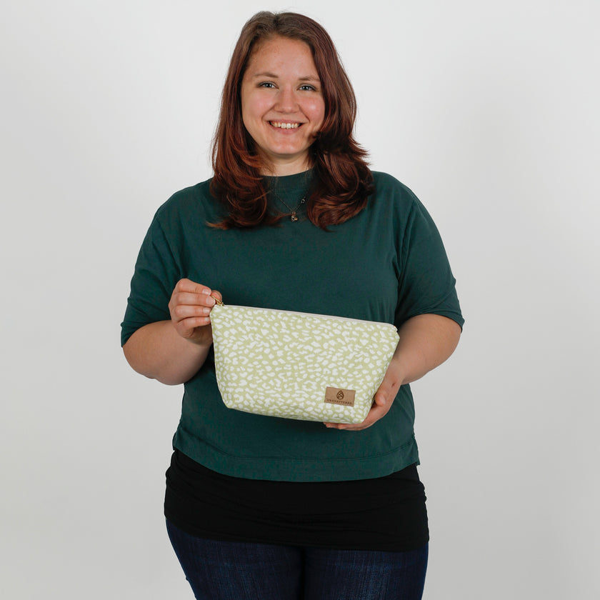 Woman holding a green and white patterned makeup bag against a plain background named after Sky
