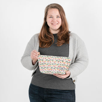 A woman holding a multicolor confetti puff plush makeup kit with a gray label named after Stasia 