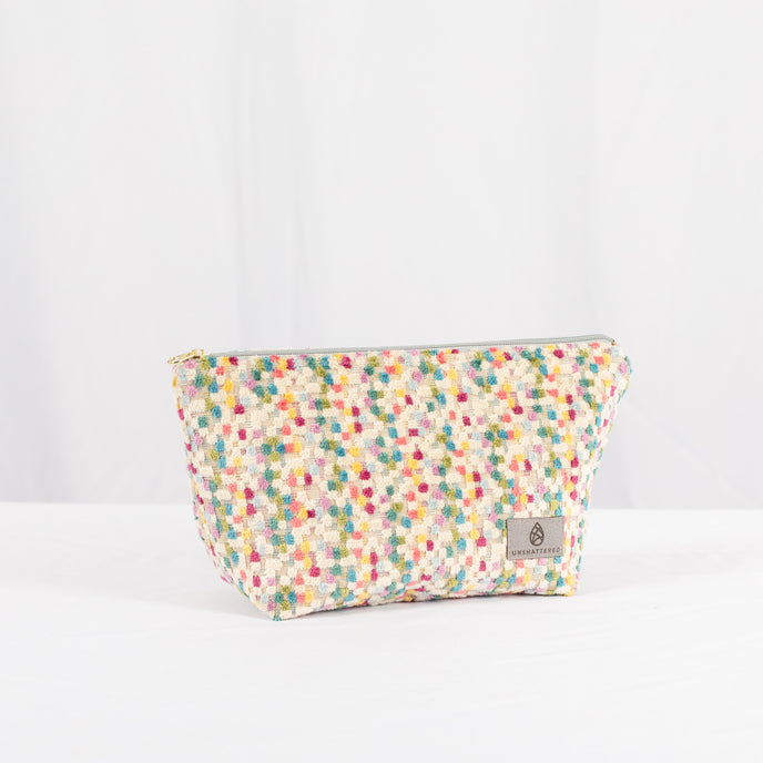 A multicolor confetti puff plush makeup kit with a gray label and gold tone hardware 