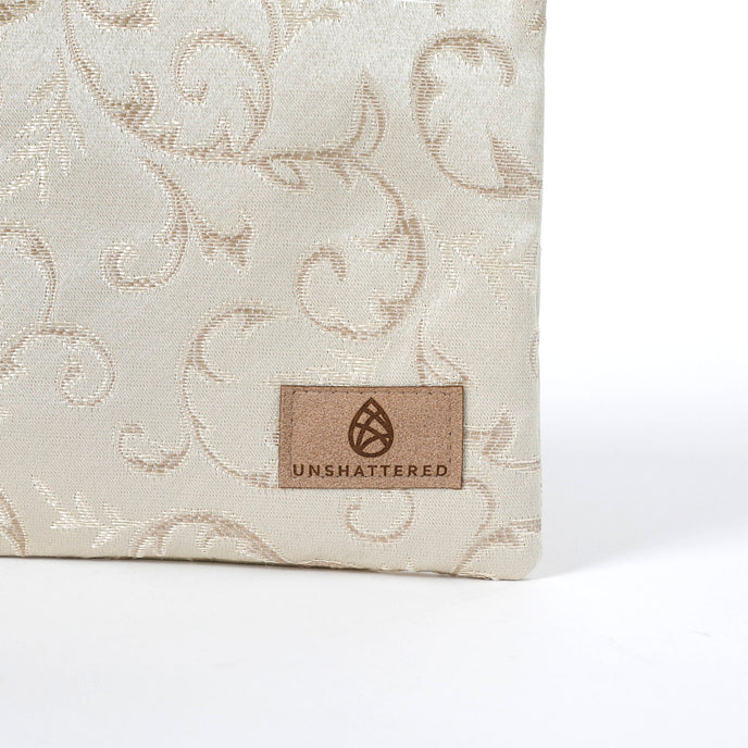 Tan suede label on a beige fabric zippered pouch with intricate patterns on a white background