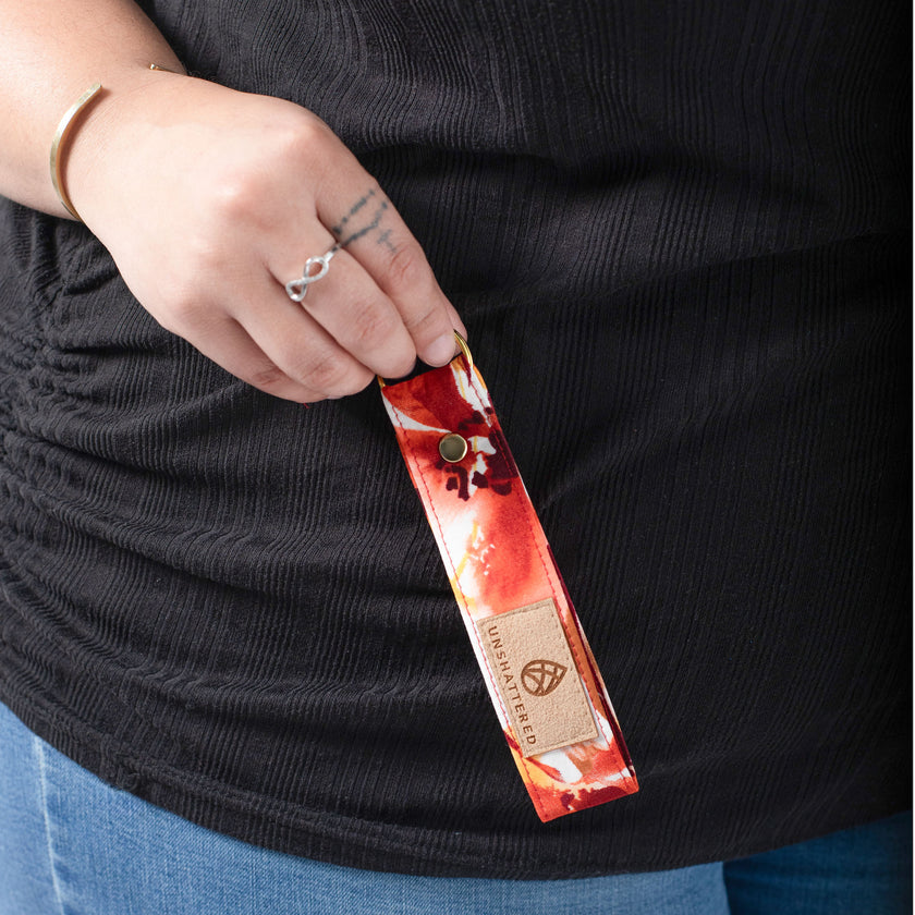 A woman holding a red flower fabric loop keychain with a tan label and gold hardware 