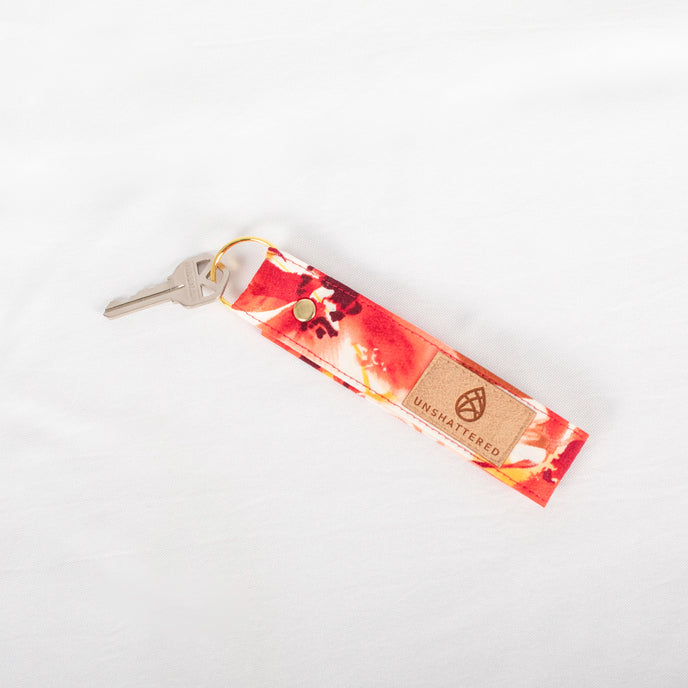 A gold-tone keyring attached to a red and orange floral patterned keychain with a label that reads Unshattered name after Susana.