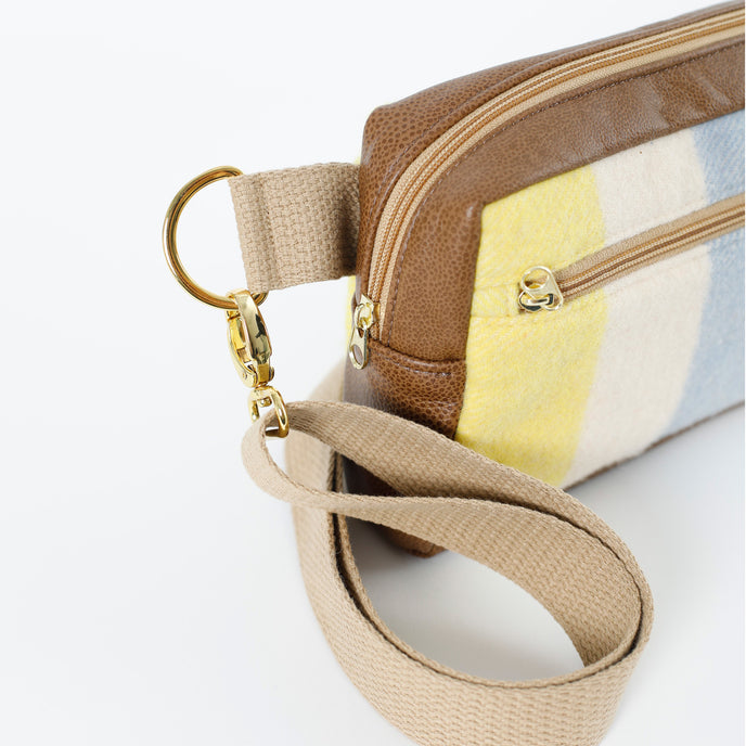 A tan strap with gold hardware on a wool yellow, white and blue errand bag with brown luxury leather alternative accents