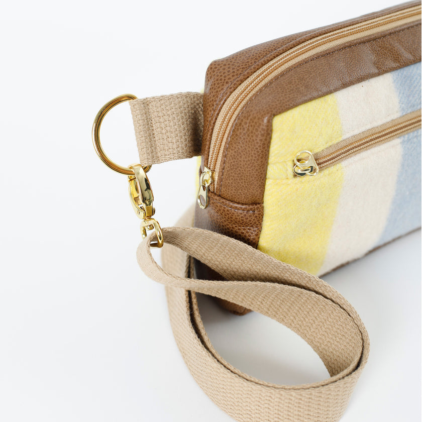 A tan strap with gold hardware on a wool yellow, white and blue errand bag with brown luxury leather alternative accents