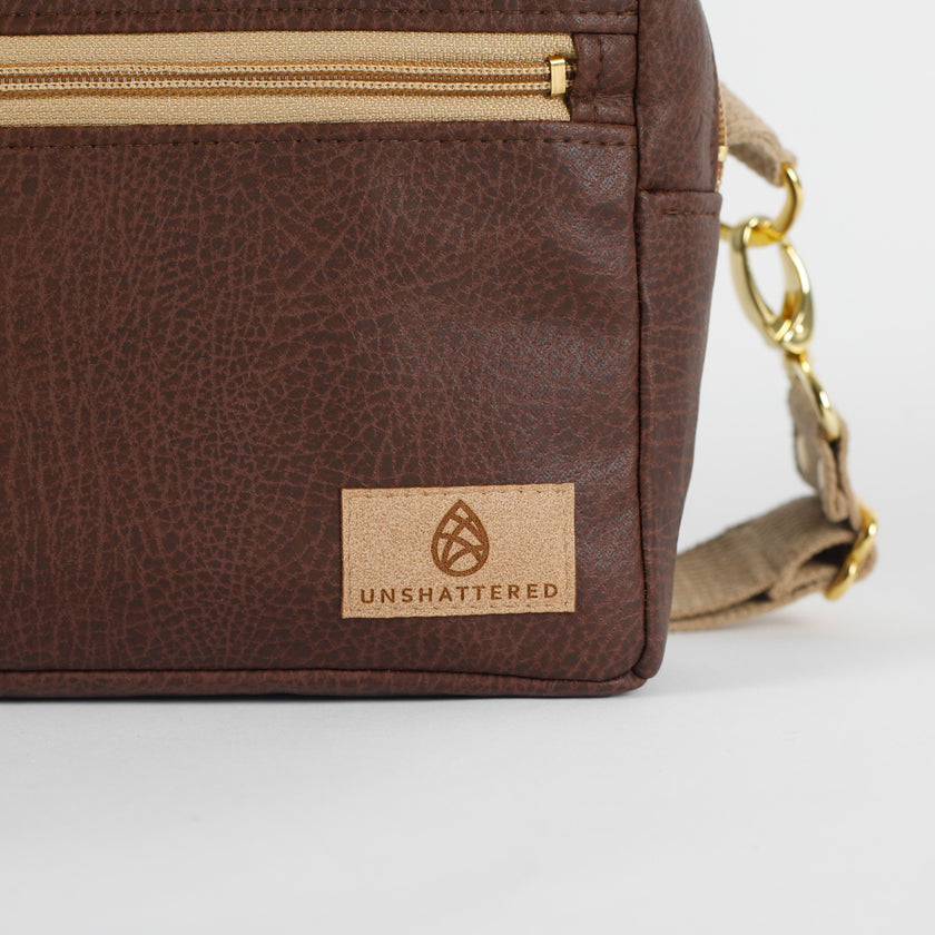 Close up of tan suede Unshattered label on a brown vegan leather bag on a white background named after Priscilla.